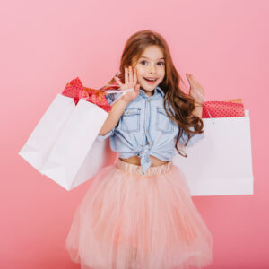 pretty-joyful-young-girl-tulle-skirt-with-long-brunette-hair-walking-with-white-packages-pink-background-lovely-sweet-moments-little-princess-pretty-friendly-child-having-fun-camera